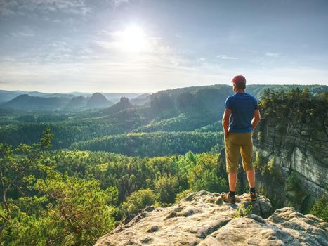 Man on a stone observing the landscape. Lonely young sportsman stands on the mountain and looks into the far distance 