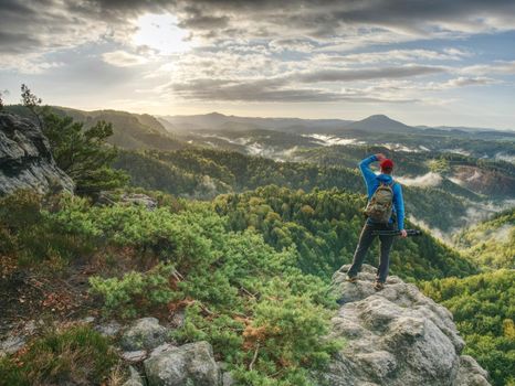 Freelancer create nature photos. Professional photographer takes photos with camera on tripod on rocky peak. Dreamy fogy landscape