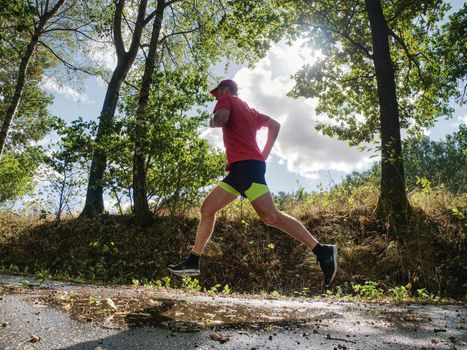 Man runner in yellow black shorts pants and red t-shirt is jumping over pool on asphalt road. Evening fitnes exercise in fall park