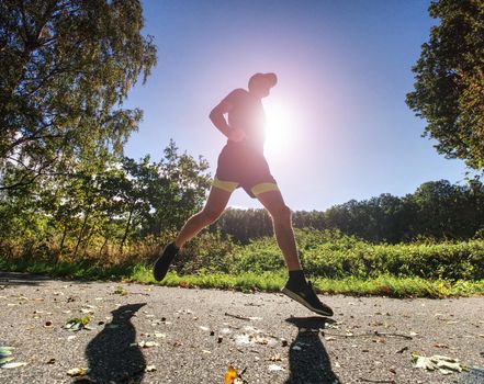 Exigent physical training. The athlete runs fast through alley. Wet asphalt with fallen maple and spen  leaves