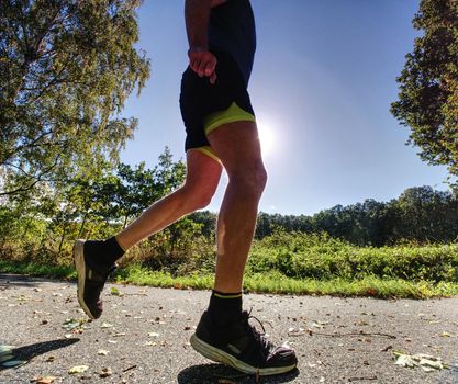 Slim body guy runs on path with fallen leaves. Warm day for outdoor excersising. 