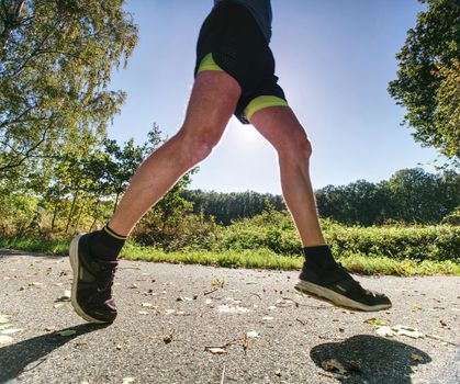 Man running on asphalt track. Athlete running fast in a park with dense trees in the background.