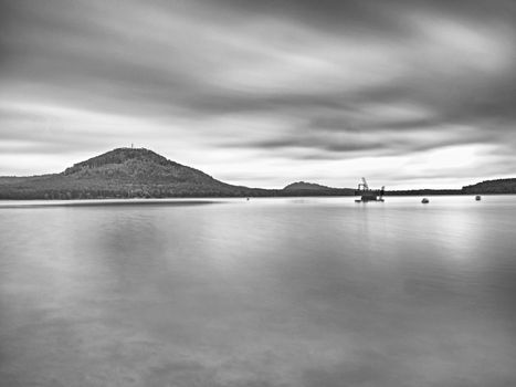 Autumn view over  low level pond to forest hill on opposite bank. Autumn melancholic atmosphere. Long exposure.   Black and white photo.