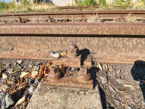 Detail of rusty screws and nut on old railroad track. Wooden oiled tie with rusty nuts and bolts. Damaged surface of rail rod. 