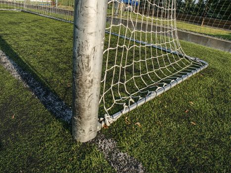 Hang bended white soccer net in  soccer football net. Grass and white painted line on football playground in the background