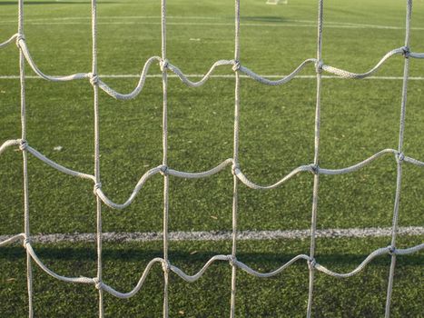 Hang bended white soccer net in  soccer football net. Grass and white painted line on football playground in the background