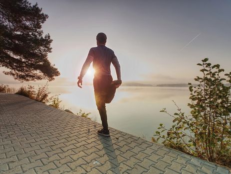 Runner stretching Leg in front of river. Athletic sport man stretching leg muscles before run and jog in nature training workout 