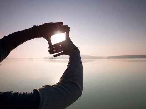 Fingers gesturing picture frame on sunrise seaside. Sunlight on beach. Sunset at the sea. Hand-made gesture in love concept.