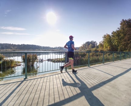 Man is training in the nature with sun behind him. Young man on morning run outdoors.