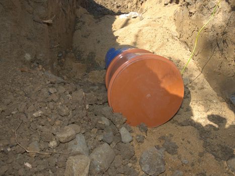 New plastic tube for portable water with safety cover in a trench dug.  Blue plastic bent pipe ready for welding in a trench of sand.