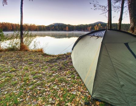 Tent on romantic place at lake shore. Colorful fall forest. Hilly horizon with last sun beams.