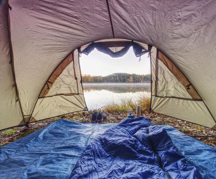 Tent on romantic place at lake shore. Colorful fall forest. Hilly horizon with last sun beams.