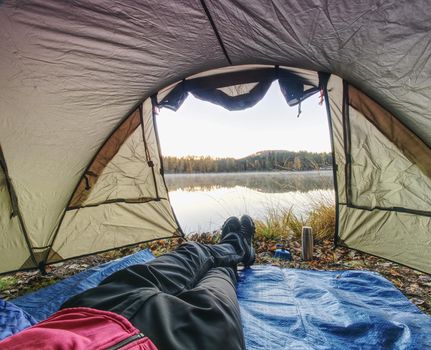 View over man body in camping tent to lake in beautiful morning. Enjoy freedom in pure nature.