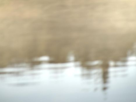 Lake water is mirroring forest on oposit bank. Romantic abstract blurry view to water level.