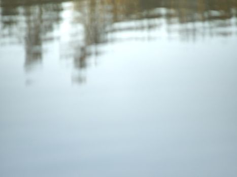 Mirroring of treetops in lake water level. Gentle mist above water in orange shadows from daybreak sun.