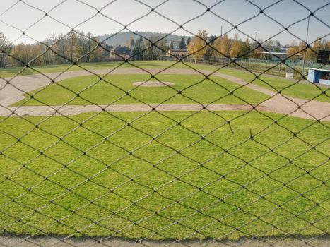 Empty baseball green field view grandstand.  View through safety net around baseball field on sunny day