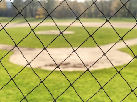 Youth baseball field viewed from behind home net in morning light.