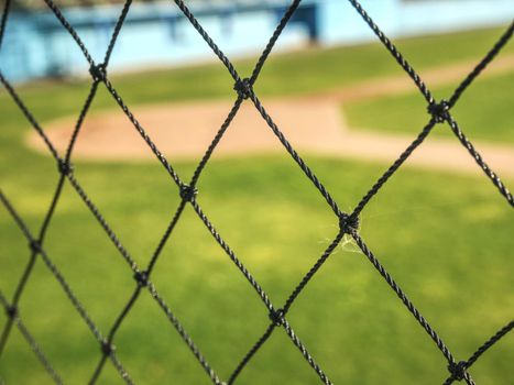 Empty baseball green field view grandstand.  View through safety net around baseball field on sunny day