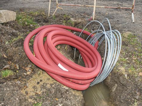 Red ribbed protective pipe with steel cable inside. Hole in the park