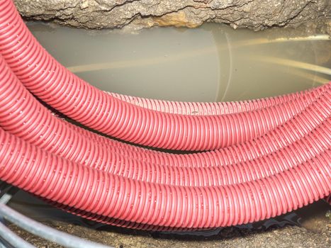 Red ribbed protective pipe with steel cable inside. Hole in the park