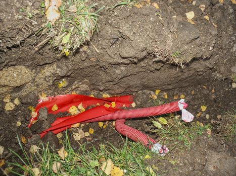 Red ribbed protective pipe with steel cable inside. Hole in the park