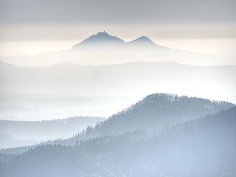 Outlines of forest hills hidden in thick mist.  Cold and damp morning in autumn nature. Unclear view to contours of hilly sides and peaks.