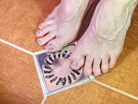 Naked feet on floor in detail. Sexy adult female legs stay on tilled bathroom floor.