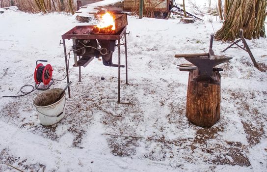 Small mobile blacksmith's forge with horse hoof inside for heating. Daily routines in horse farm.