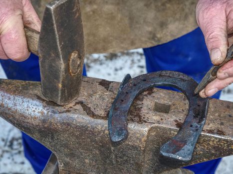 Blacksmith forging with hammer nail holes on horseshoe.