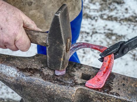 Blacksmith working hard to finalize horseshoe. Smithy process on the anvil. Hammering of glowing steel.