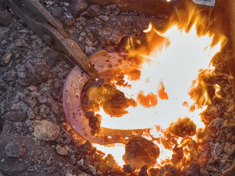 Craftsman blacksmith warming iron to create  horseshoe in the fire and on the anvil