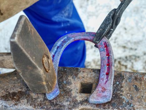 Detail of making new horseshoe in blacksmith workshop. Male farrier hammers a nail into a horseshoe