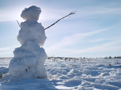 Real icy snowman standing in winter landscape. Hot spring sun and some people walk at horizon