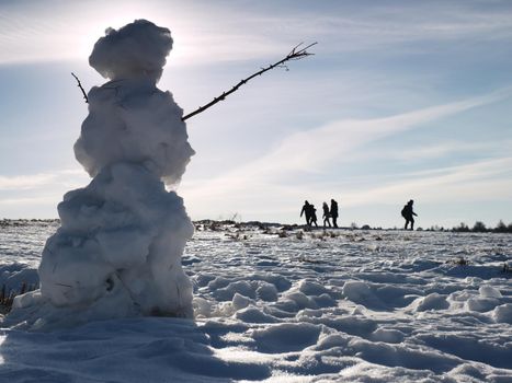 Man walk at icy snowman melting on last snowy place on spring hill. Sunny spring day