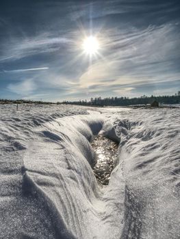 Hole in icy snow with sun flares. Lovely winter scene.