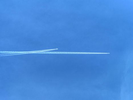 Sunny blue clear sky with white smoke trails of flying plane. Airplane crosses the contrail of another aircraft