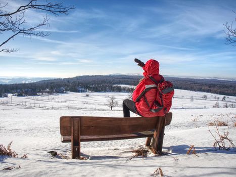 Side view of man walking in snow on winter day, mountain landscape. Hiker in red with  red backpack. Winter hiking travel concept. 