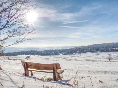 Winter landscape, sunny day. Footprints in the fresh snow lead to a wooden bench