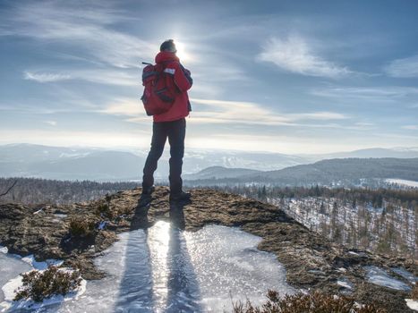 Standing man with raised arm on icy stone and looking on snow covered mountains. Landscape with traveler, 