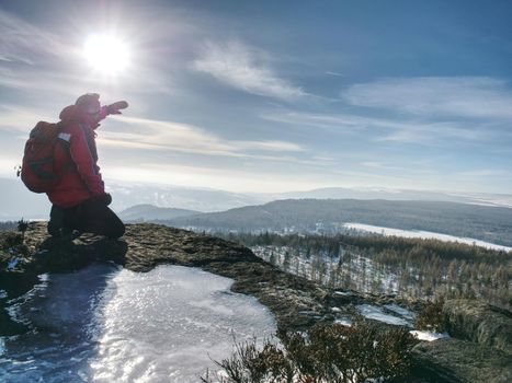 Standing man with raised arm on icy stone and looking on snow covered mountains. Landscape with traveler, 