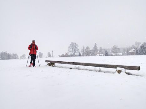 Winter snowshoing in fresh snow. Woman walk whiel snow falling from heavy grey clouds, windy cold weather.