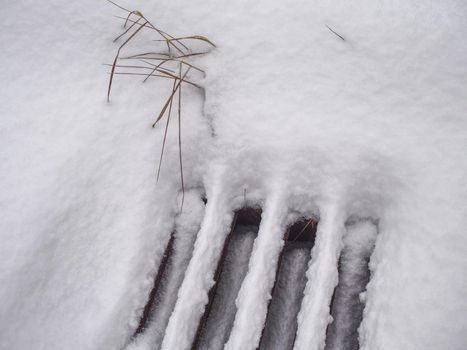 White snow on metal grate outside pavement road. White snowflakes flows into the manhole. Pollution metaphor