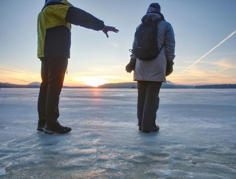 Cute couple in bay of frozen sea. They hold together at the frozen pond near sandy beach