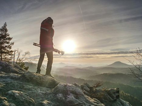 Hiker and photographer stay with tripod on cliff and takes photos. Two people stay at  tripod on the background of a mountain range and sky with clouds 