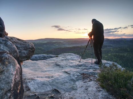 Professional photographer takes photos with camera on tripod on rocky peak Tourist with camera and tripod in cold weather