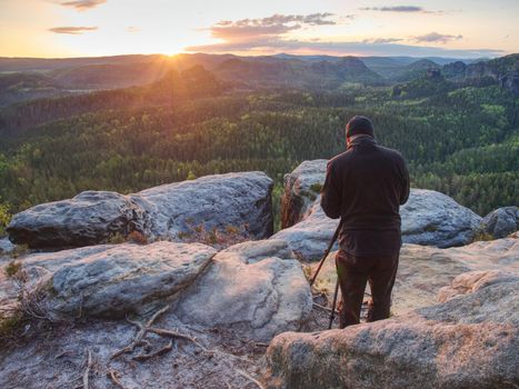 Nature photographer hold tripod with camera. Man at sunrise at open view on mountain peak blue sky