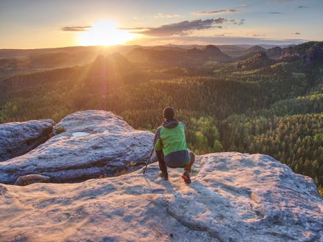 Photographer is setting tripod and camera for an art work.  Professional photographer takes photos with camera on tripod on rocky peak