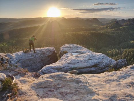 Nature photographer hold tripod with camera. Man at sunrise at open view on mountain peak blue sky