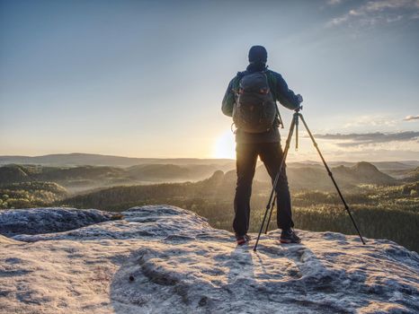 Artist set camera and tripod to photograph the sunrise on a rocky summit. Artist works in nature