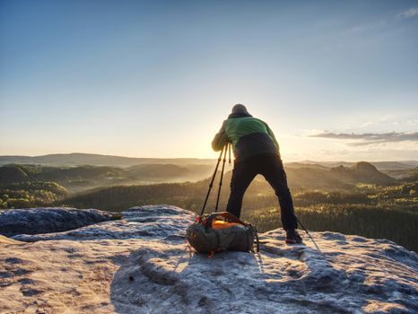 Artist set camera and tripod to photograph the sunrise on a rocky summit. Artist works in nature